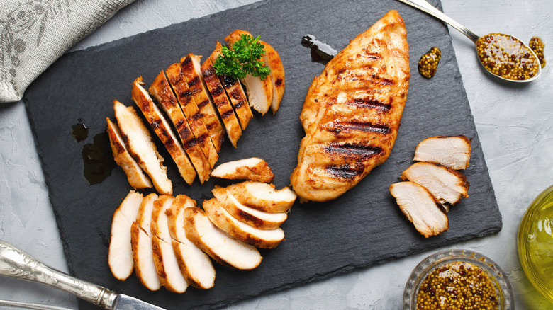 Marinated chicken has been grilled and then sliced on a cutting board.