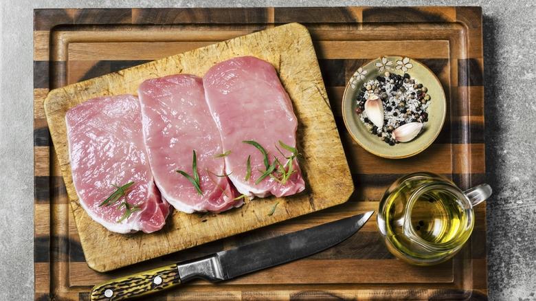 Three raw pork chops on a cutting board.