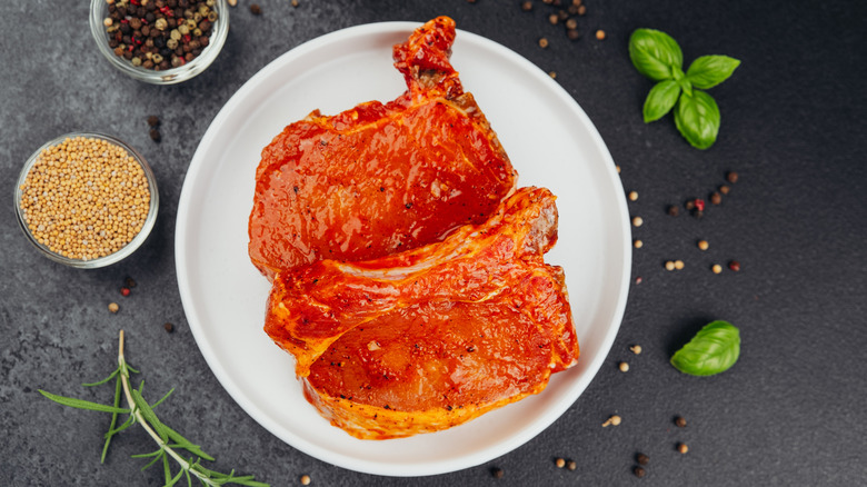 Marinated pork chops alongside mustard seeds and peppercorns.
