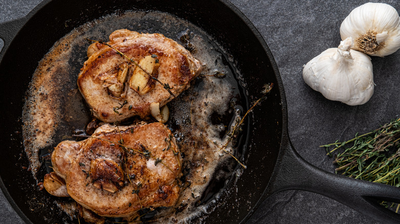 Pan-seared pork chops cooking in a skillet.