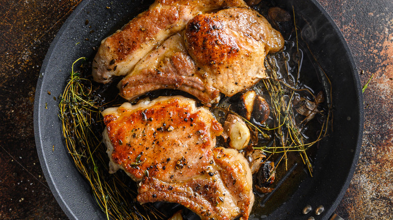 Pork cutlets in a pan with garlic and herbs.