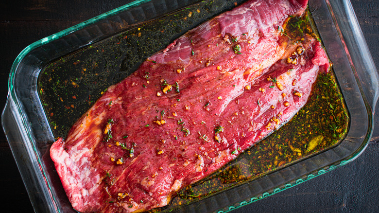 A big piece of steak bathed in marinade in a clear casserole dish