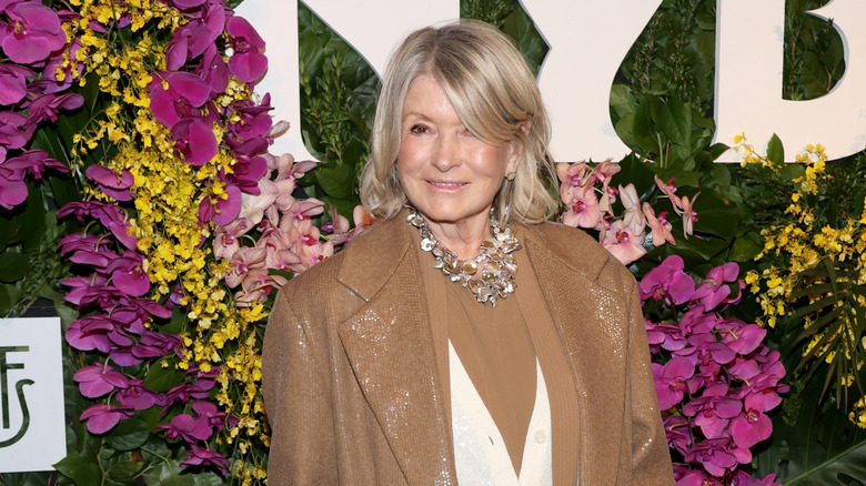 Celebrity chef Martha Stewart appears in front of a colorful wall of flowers at an event.