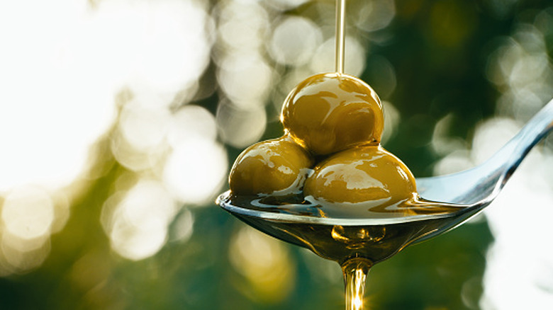 Olives on a spoon with olive oil being poured on top