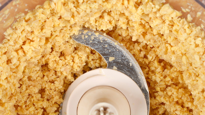 Coarsely ground soybeans and a blade inside a food processor bowl.