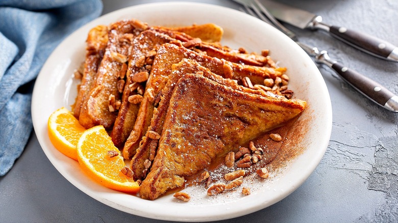 Half slices of French toast topped with cinnamon, chopped pecans, and orange slices on a white plate