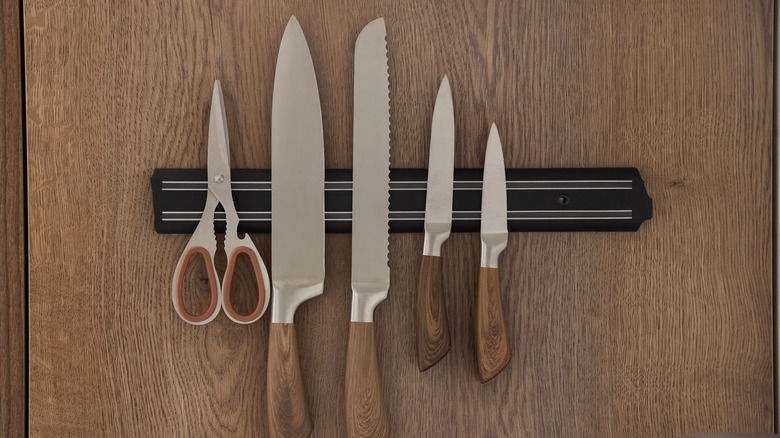 An assortment of knives organized on a magnetic strip including a chefs knife, serrated knife, and paring knife.