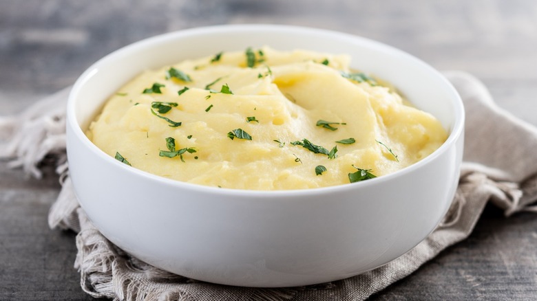 A white bowl of creamy mashed potatoes with chopped greens
