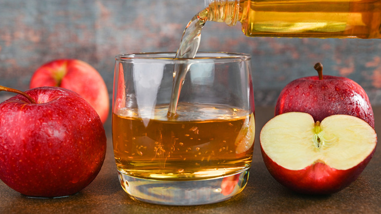 Apple cider being poured into a glass that's surrounded by apples