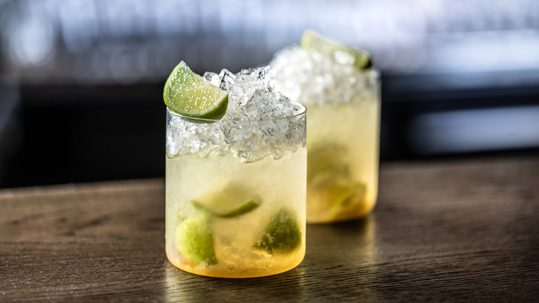 Two cocktail glasses filled with ice, limes, and juice