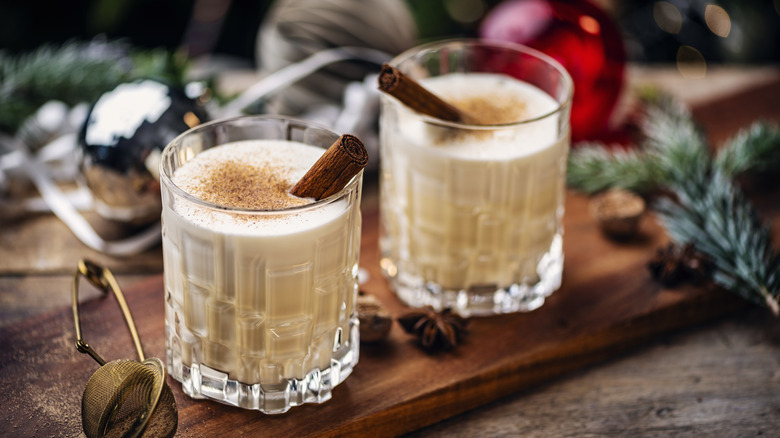Two glasses of eggnog with cinnamon garnish and Christmas props