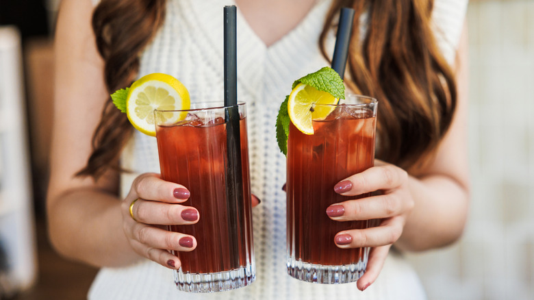 A person holding two iced teas with lemon garnishes