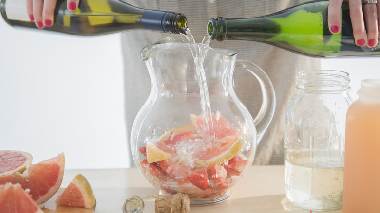 A person mixing wine in a fruit-filled pitcher to make sangria