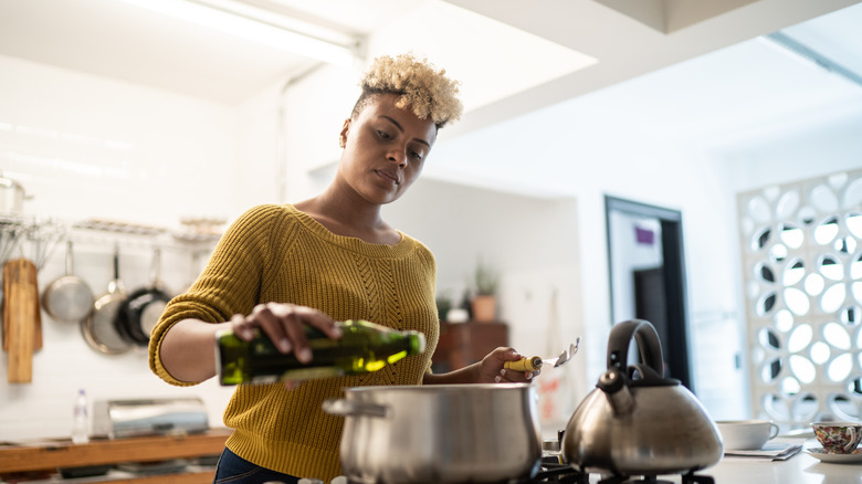 woman cooking food on stovetop using bottle of oil