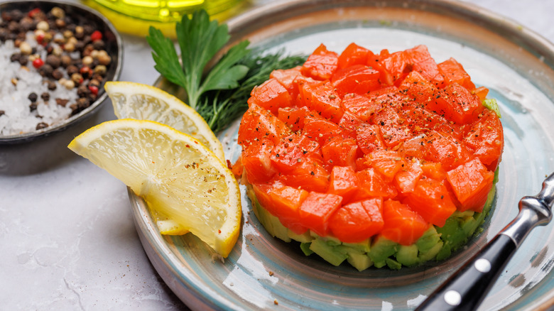 Salmon tartare tops diced avocado beside lemon wedges on a plate.