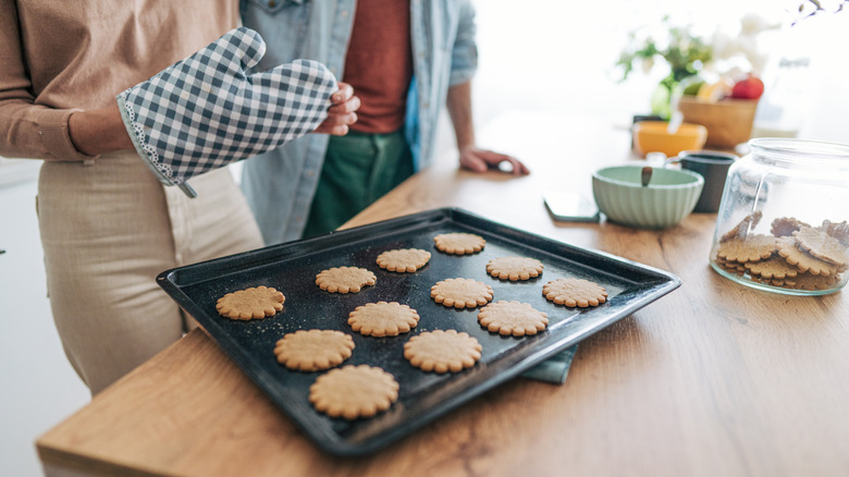 Cookies on a baking sheet sitting on top of a wooden kitchen island; a person wearing an oven mitt is also in the frame.