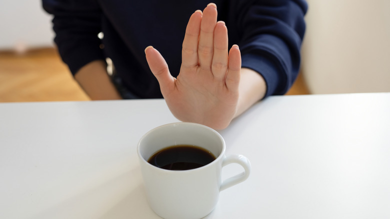 Person holding their hand in a "stop" motion in front of a cup of coffee