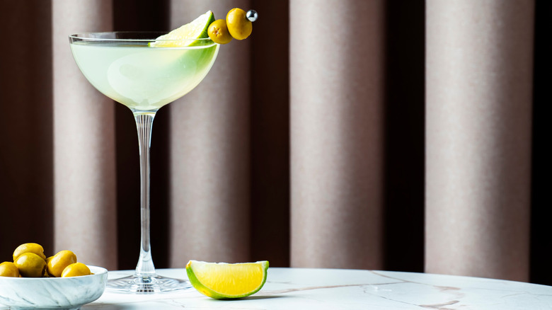 A dirty margarita with lime wedges and olives.