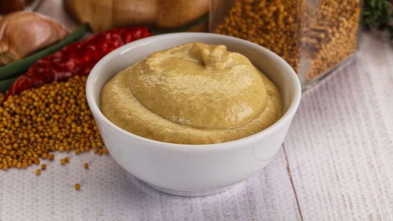 A white bowl of dark gold Dijon mustard.