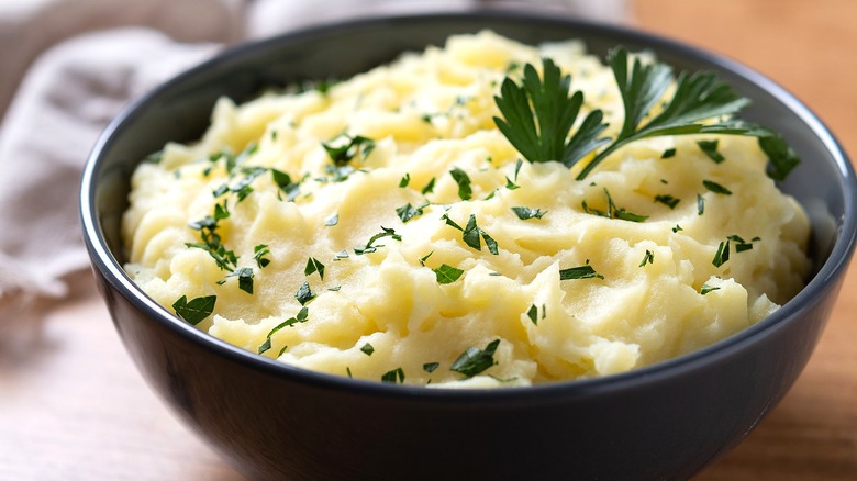 Mashed potatoes topped with chopped Italian parsley in a black bowl