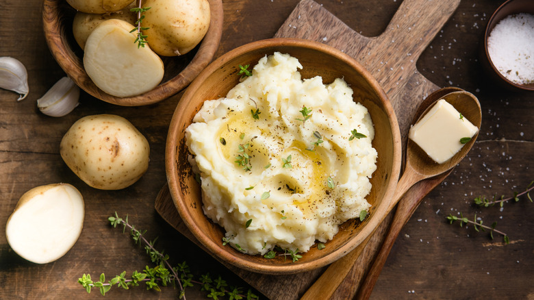 Creamy mashed potatoes with raw potatoes and spices on a rustic background