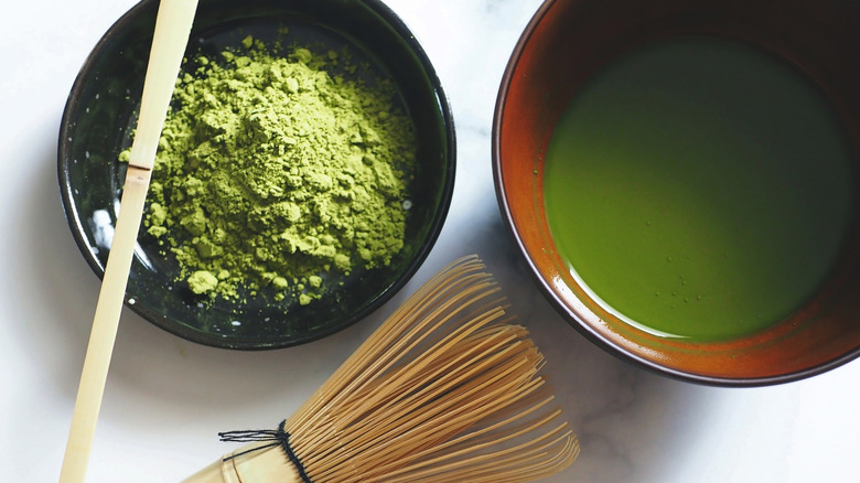 matcha powder next to a matcha whisk and brewed tea