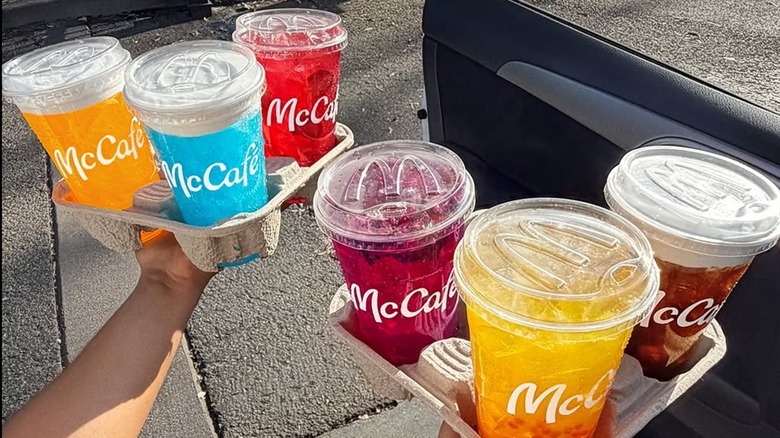 Person holding two cardboard drink holders of colorful McDonald's McCafe sodas