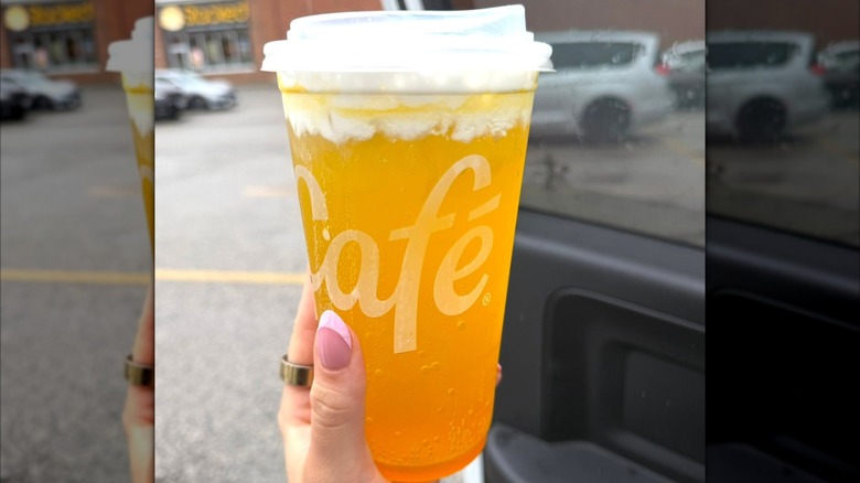 Person's hand holding an Orange Dream with Hi-C drink in a plastic cup