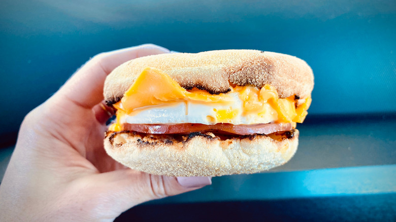 Person Holding Breakfast Sandwich with Egg Ham Bacon and Cheese on Toasted English Muffin