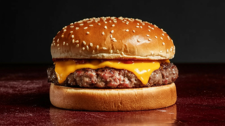 Close-up photo of a cheeseburger sitting on a shiny dark red surface