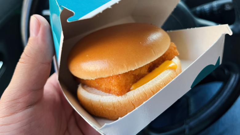 A person holding a Filet-O-Fish sandwich in its opened box, in a car