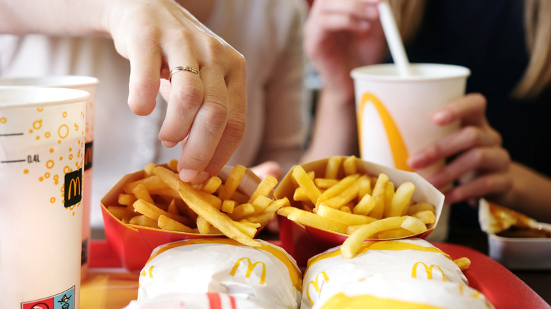 Person's hand grabbing fries off a McDonald's tray holding fries, burgers, and drinks