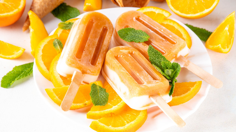 Three orange creamsicle treats on a plate of oranges and mint