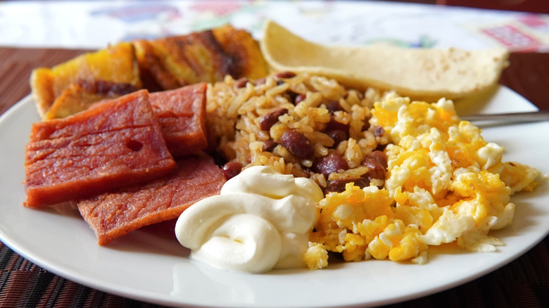 A Nicaraguan breakfast features eggs, plantains, rice, breads, tortilla, and crema.