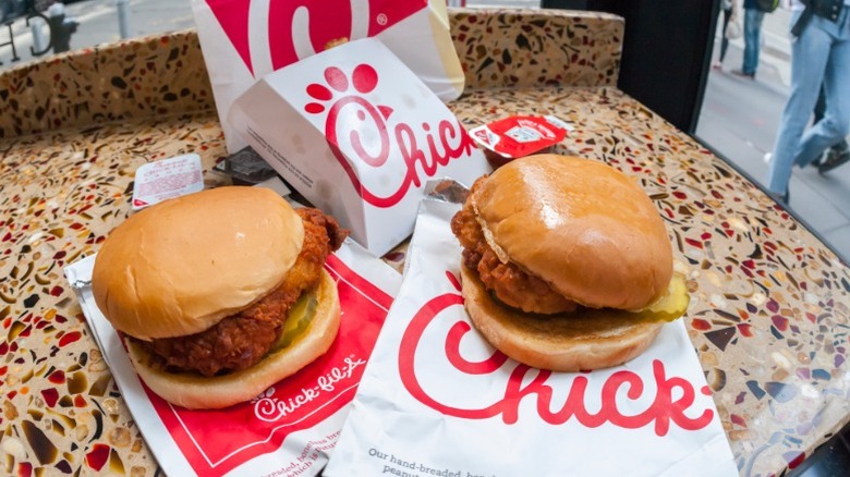 Two chicken sandwihes from Chick-fil-A sitting beside one another on a counter on top of Chick-fil-A packaging.