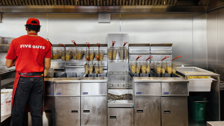 A fry cook at Five Guys stands behind a line of deep fryers ready to cook fries to order