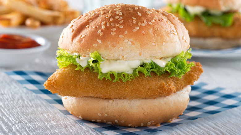 Breaded fish sandwich with lettuce and tomato on a sesame seed bun