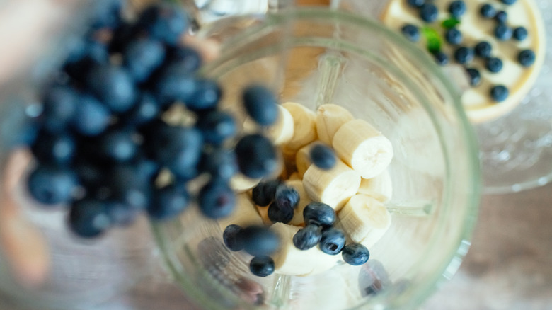 smoothie ingredients like bananas and blueberries going into a blender