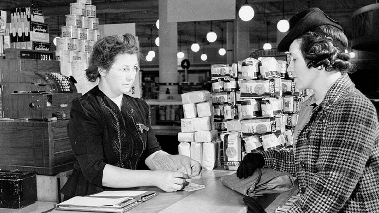 Black and white photo of a woman using ration stamps during a grocery store purchase.