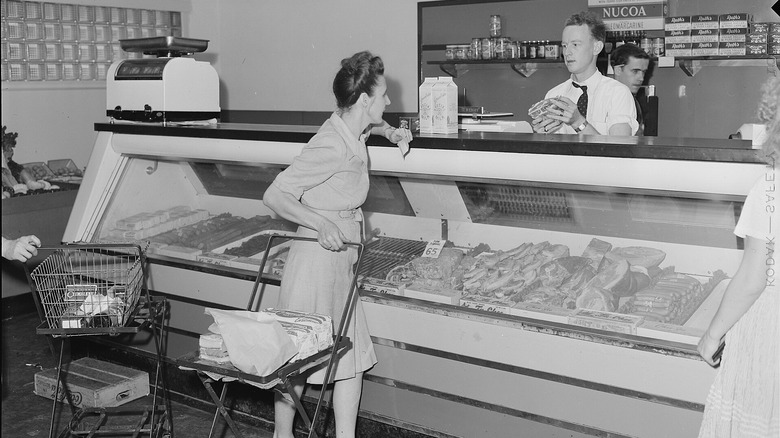 Black and white photo of a woman in a dress ordering meat from a butcher.