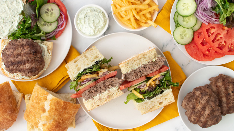 Overhead shot of a, halved, well-stacked gyro burger with toppings and condiments on the side.