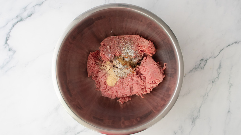 A large bowl with ground meat sprinkled with an assortment of spices