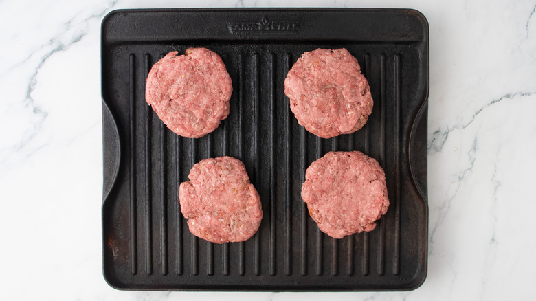 A large grill pan topped with four burger patties