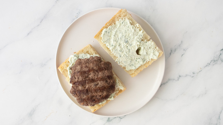 A grilled burger patty placed on a portion of loaf-style bread