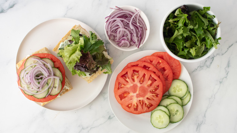 A burger topped with tomatoes, cucumbers, onions, and leafy greens