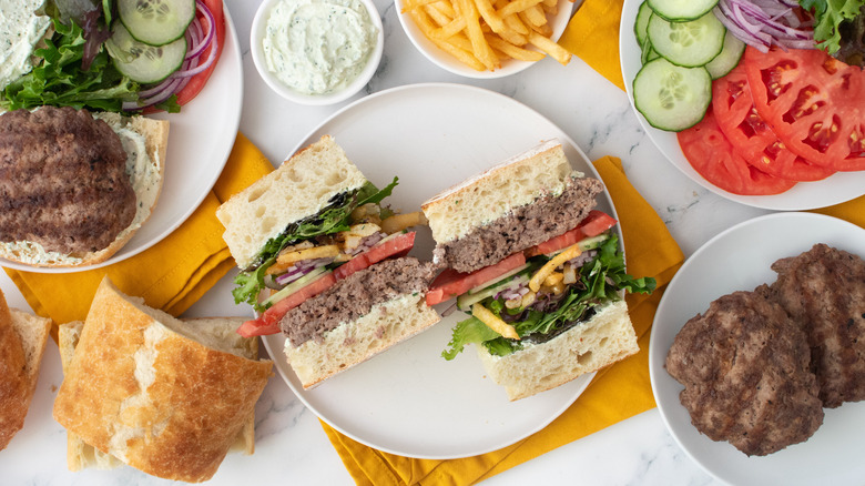 Overhead shot of a, halved, well-stacked gyro burger with toppings and condiments on the side