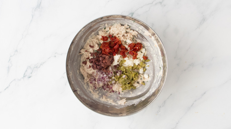 Tuna salad with olives, sun-dried tomatoes, onions, and feta in a metal bowl.