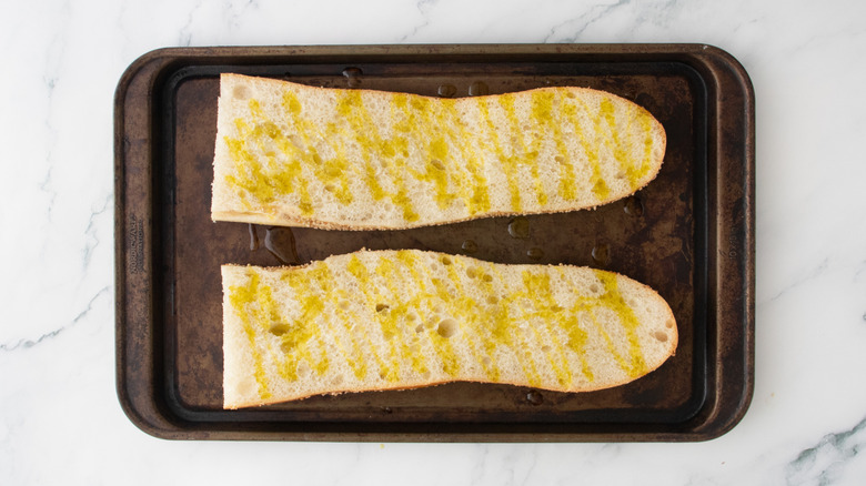 Half of a large baguette drizzled with olive oil on a baking sheet.