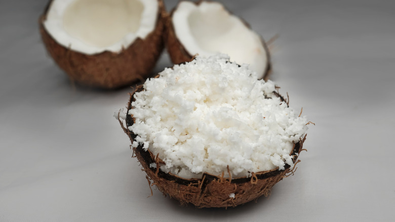 a coconut shell filled with shredded coconut with an open coconut in the background