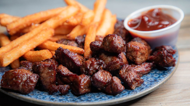 Chislic stacked on a plate with fries and ketchup in the background.